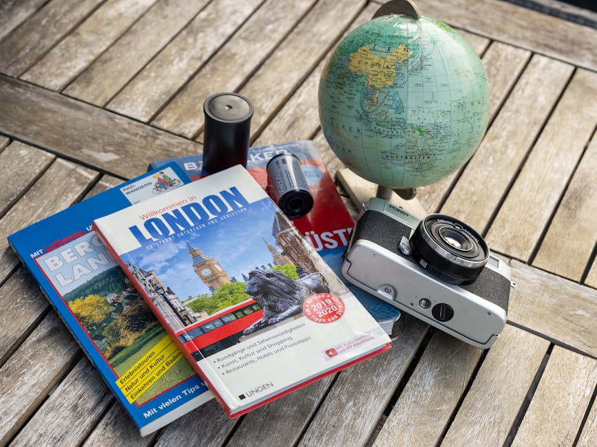 A vintage travel setup with guidebooks, a globe, and a film camera on a wooden table.